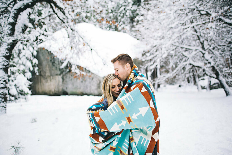 Happy couple standing wrapped in blanket in winterly landscape.