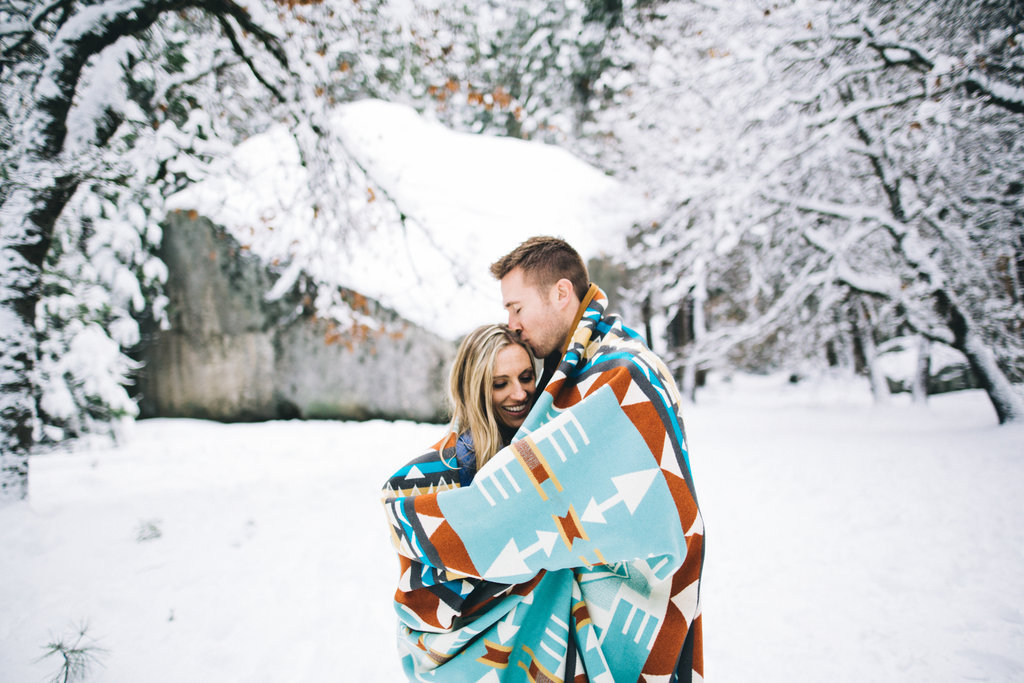 Glückliches Paar steht in eine Decke eingewickelt in winterlicher Landschaft.