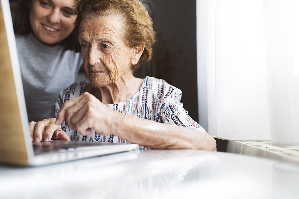 Junge und alte Frau arbeiten zusammen am Laptop.