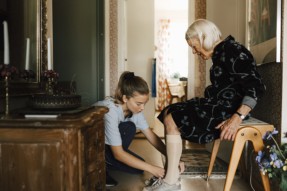Junge Frau bei der Pflege einer alten Dame zuhause